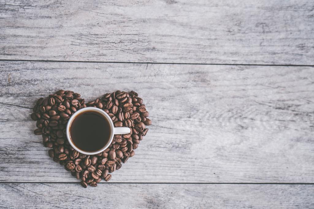 coffee beans in a heart shape with a mug of black coffee at the centre